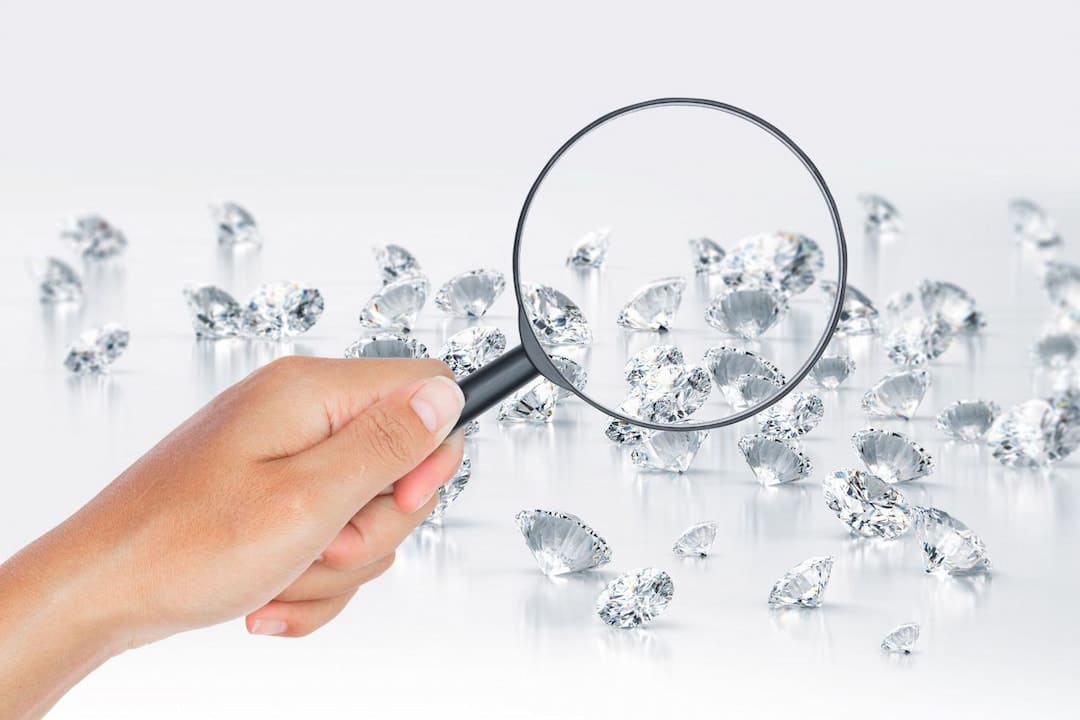 A person holding a magnifying glass above the diamonds